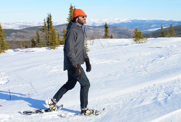 Matt is snowshoeing while wearing the burnt orange softshell Belgian cap and dark grey Milwaukee Hooded Jacket in medium