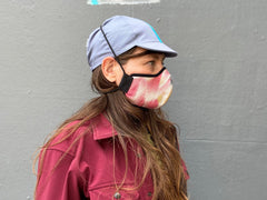 Muriel is wearing the 4-panel cotton cap in blue-grey with cyan ribbon and the cherry Shibori wing spots cotton mask