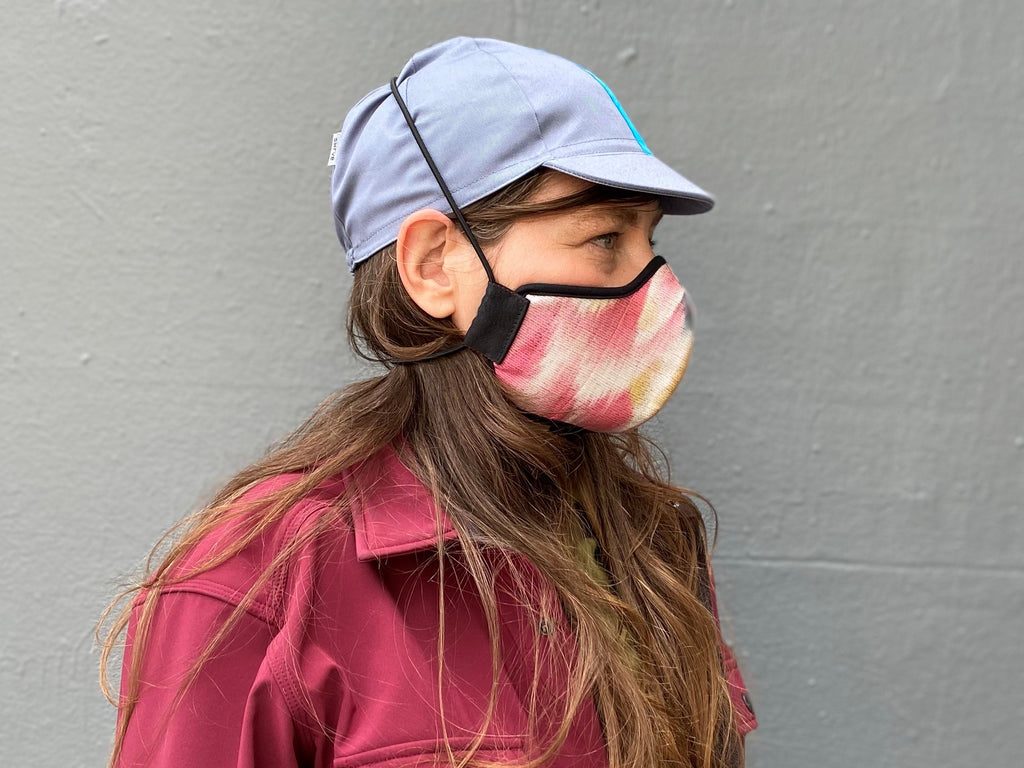 Muriel is wearing the 4-panel cotton cap in blue-grey with cyan ribbon and the cherry Shibori wing spots cotton mask